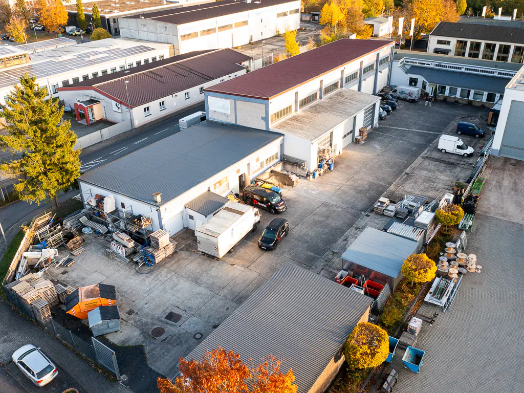 Aerial view of a commercial property with multiple buildings, vehicles, and storage areas on a sunny day.