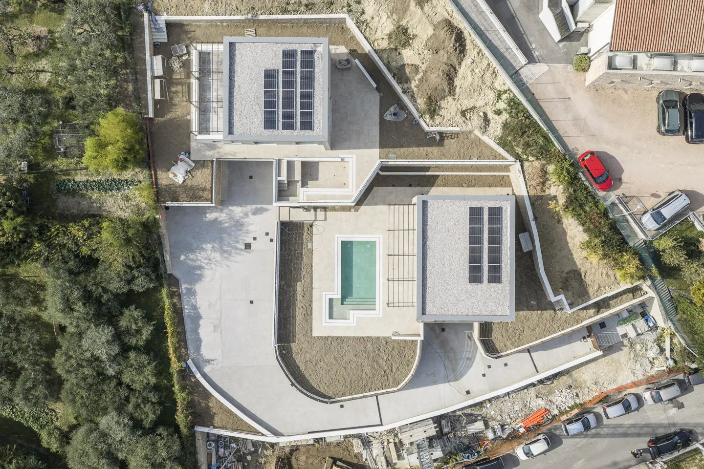 Aerial view of a modern house with a pool, solar panels, and a concrete driveway. The house is surrounded by trees and landscaping.