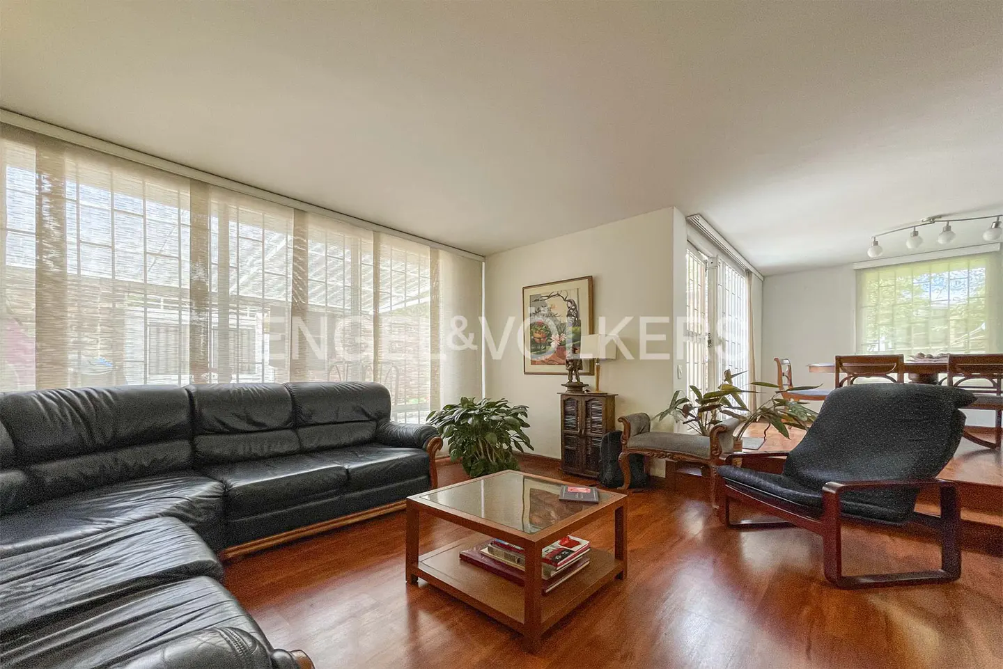 Living room with black leather sofa, wooden coffee table, armchair, and large windows with sheer curtains on wood floors.