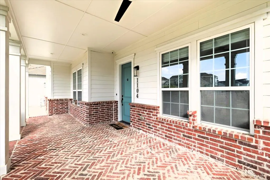 Covered porch with brick floor in a herringbone pattern, brick half wall, white siding, and a teal front door with the house number 1104.