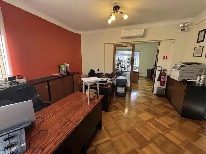 Office space with wood parquet flooring, desks, cabinets, and a red accent wall. A doorway leads to another office area.