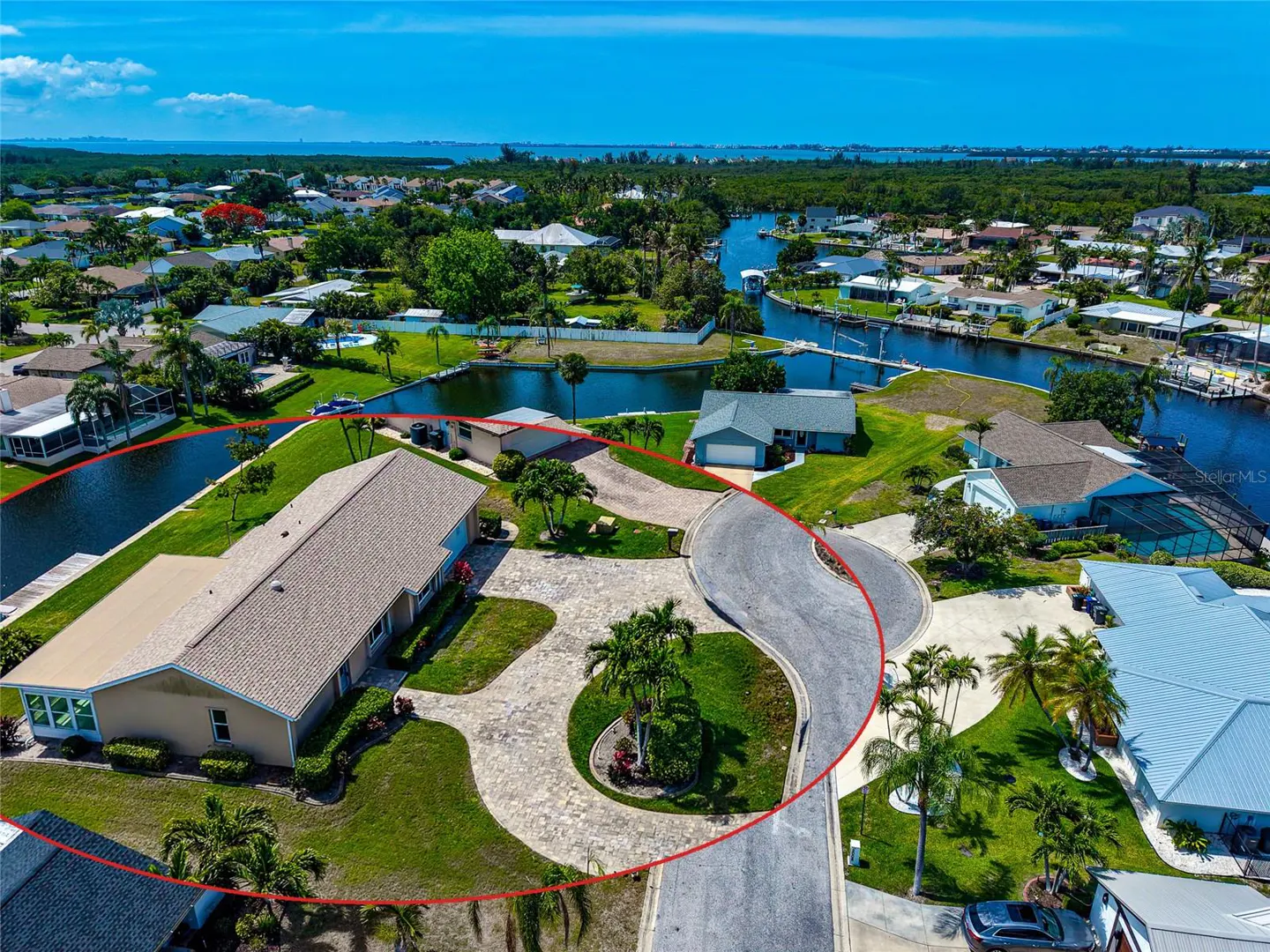 Aerial view of a tan single-story home with a beige roof, surrounded by green grass and palm trees, on a canal.