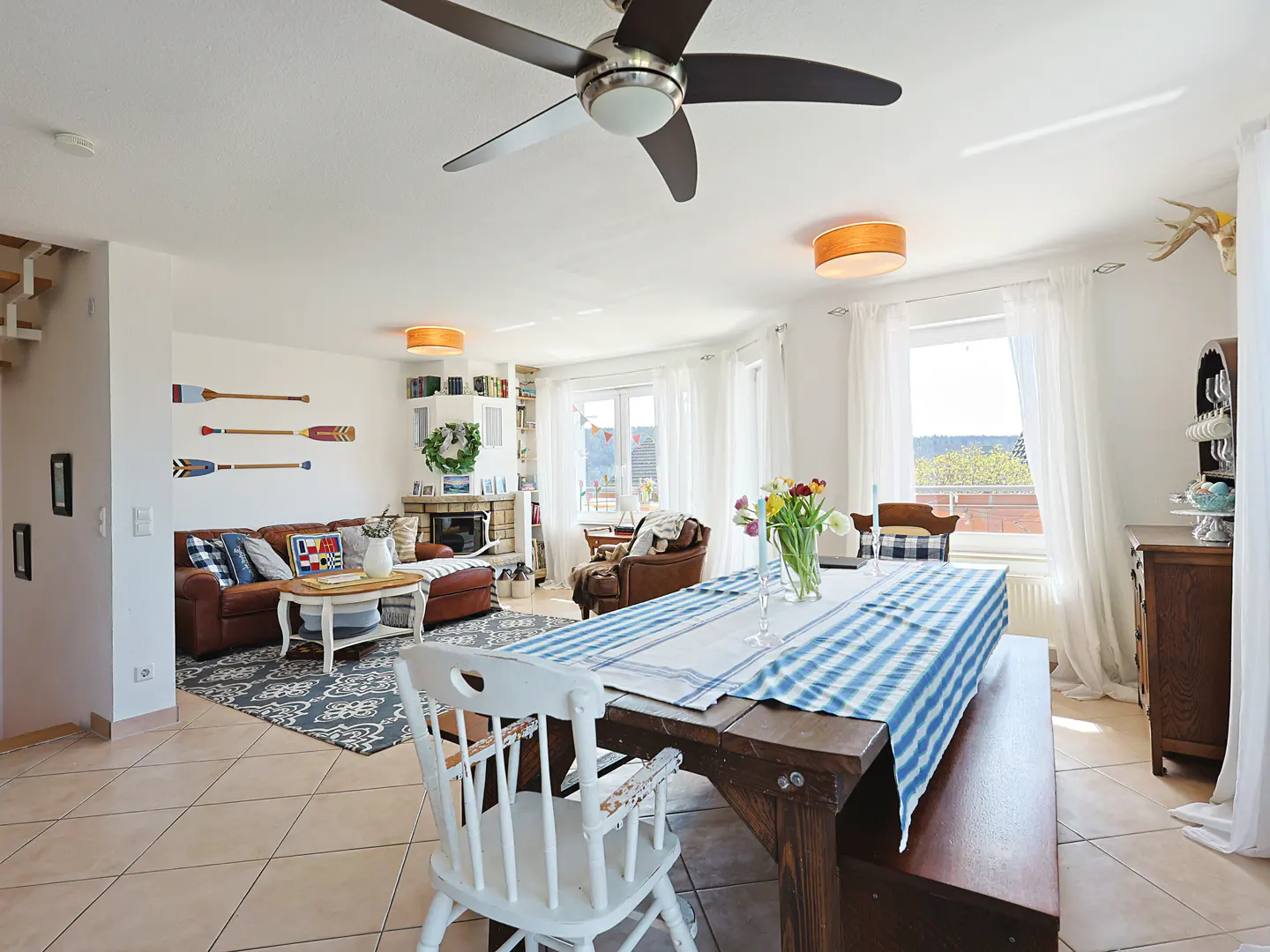 Bright living and dining area with a brown leather sofa, wooden table with blue runner, and nautical decor.