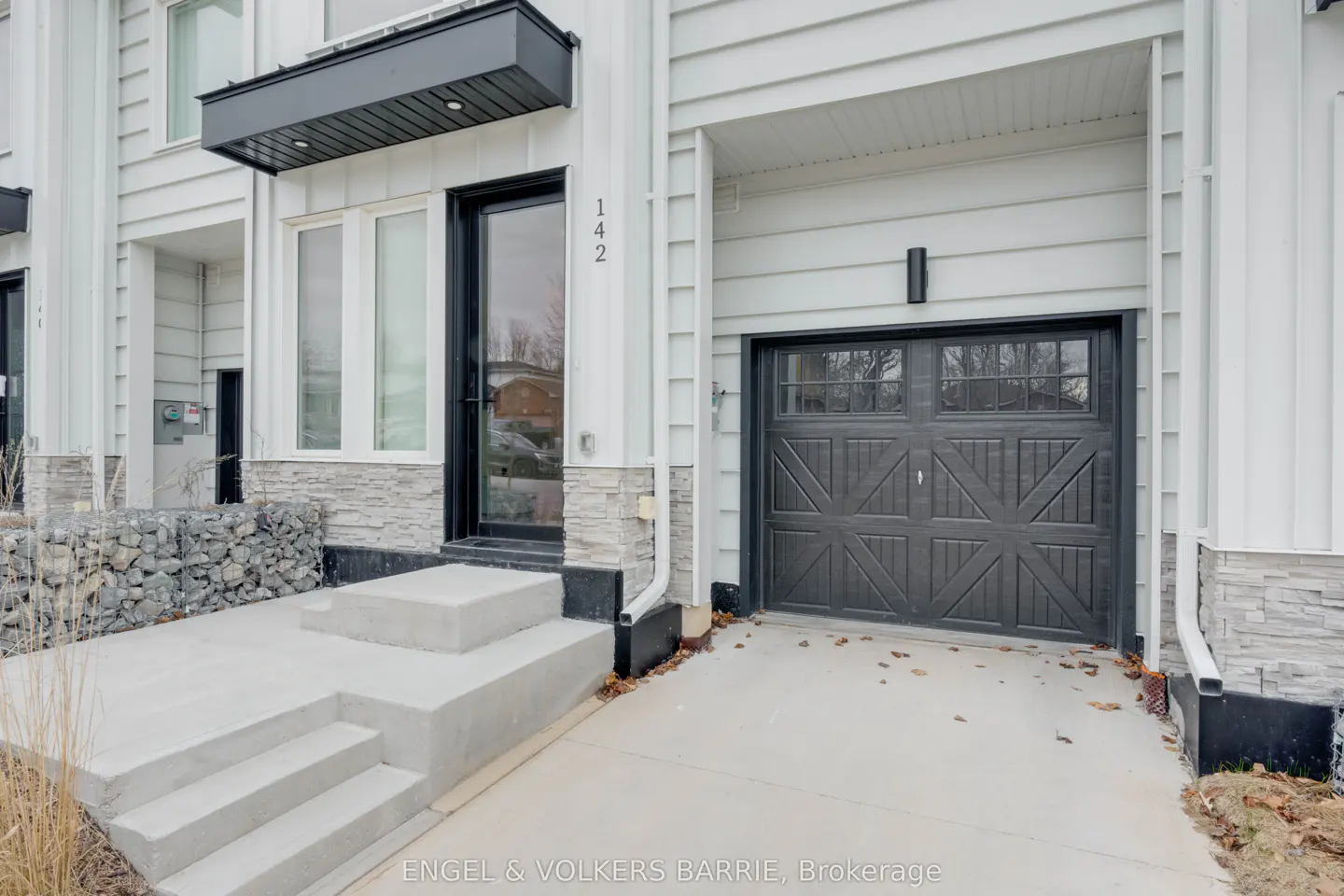 Exterior view of a modern townhouse with white siding, a black front door, and a black garage door. The house number "142" is visible above the front door.