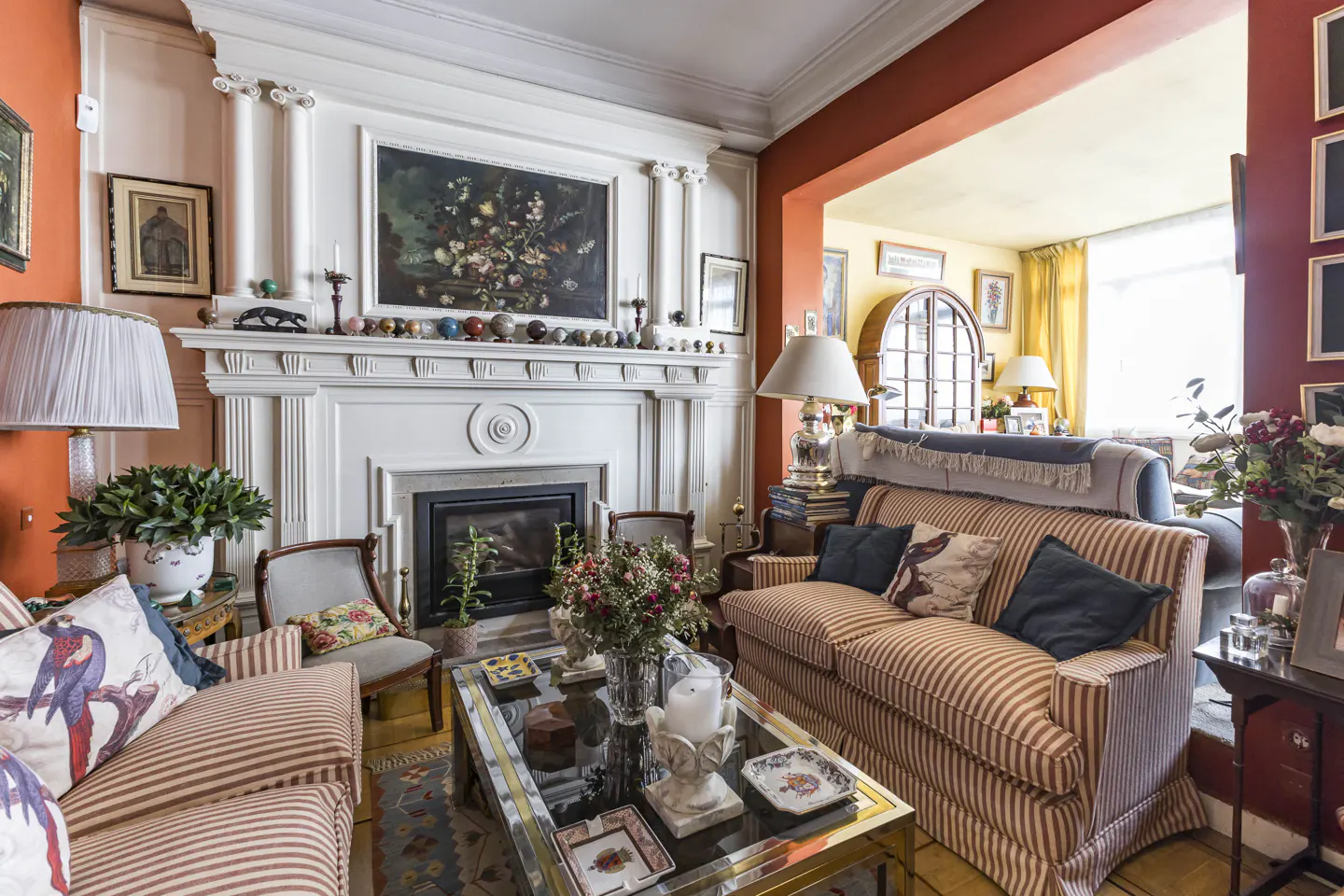 A cozy living room with striped sofas, a fireplace with a white mantel, and colorful walls.