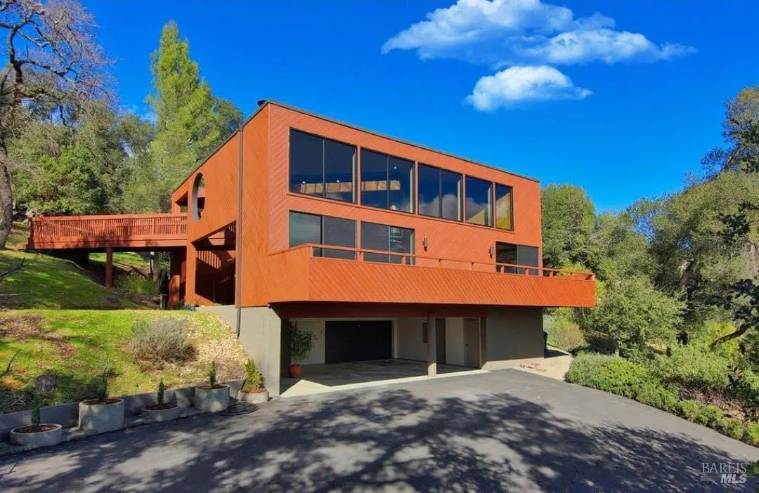 Exterior of a two-story orange house with a bridge, balcony, and a driveway on a sunny day.