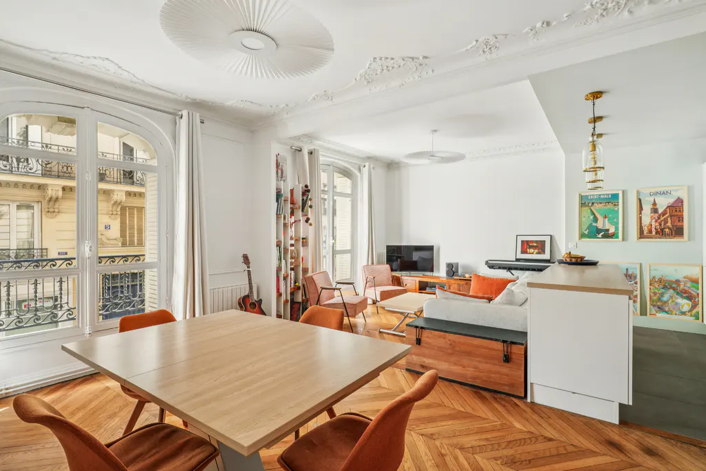 Bright, open-concept apartment with herringbone wood floors, white walls, and large windows. A dining table and chairs are in the foreground.