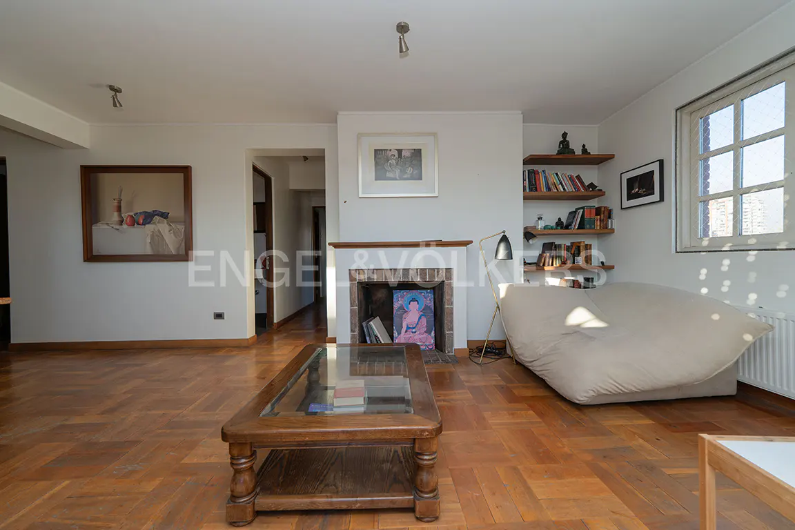 Bright living room with parquet floors, a fireplace with art, a glass-topped coffee table, and a large window.