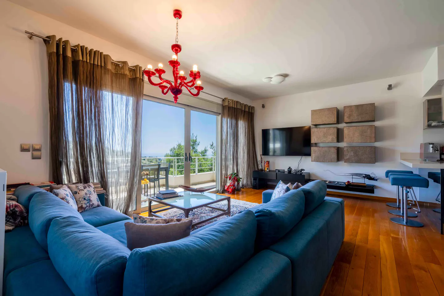 Bright living room with blue sectional sofa, red chandelier, and sliding glass doors to a balcony with a view.