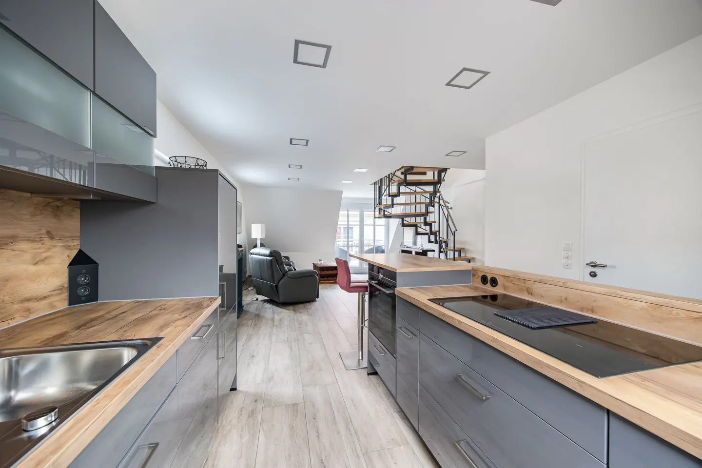 Modern apartment interior with gray cabinets, wood countertops, and a spiral staircase leading to the upper level.