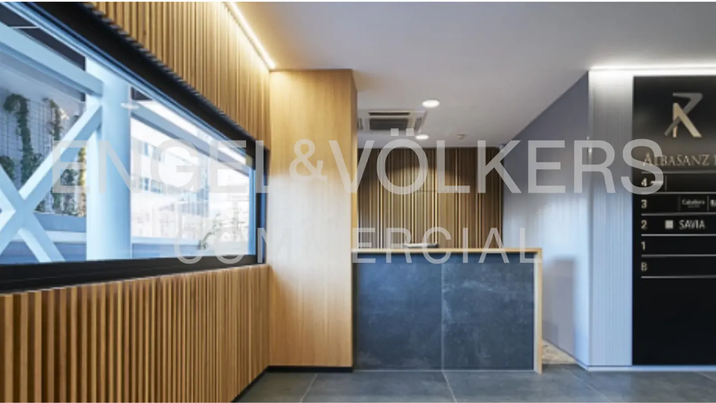 Office lobby with wood-paneled walls, a reception desk, and a directory board. A large window lets in natural light.