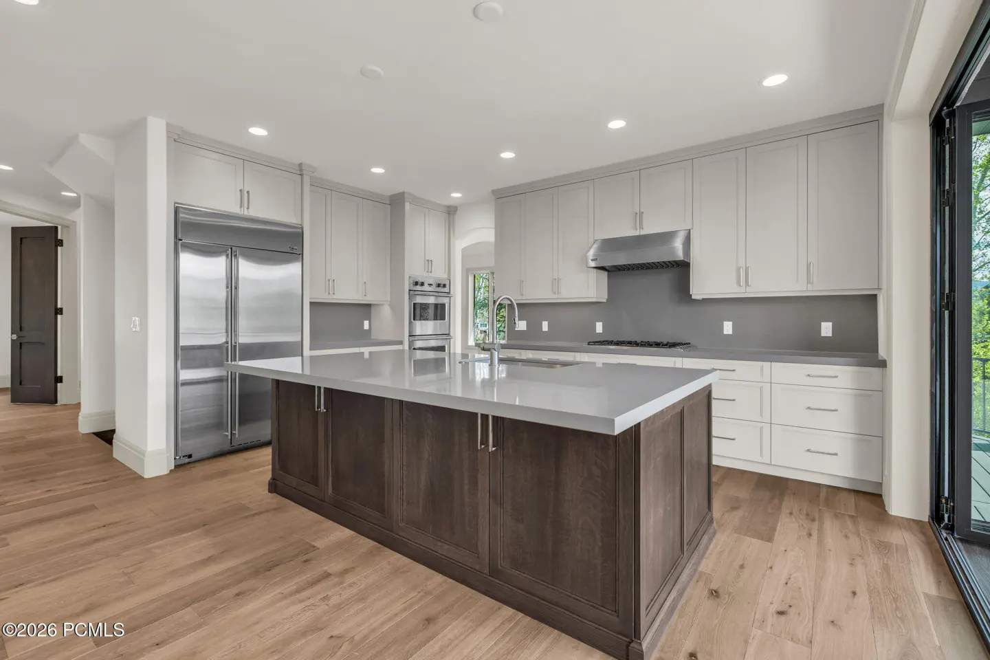 Bright kitchen with wood floors, a large island with a gray countertop, stainless steel appliances, and gray cabinets.