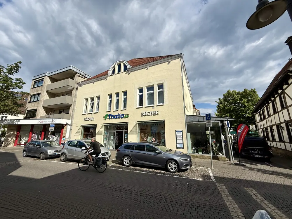 A cream-colored Thalia bookstore building on a street with parked cars, a cyclist, and a cloudy sky.
