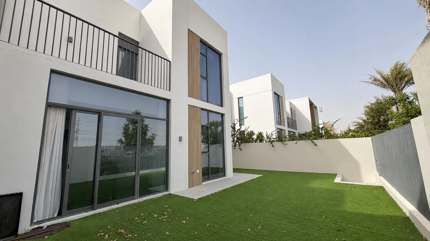 Modern white townhouses with large windows and a green lawn under a blue sky.