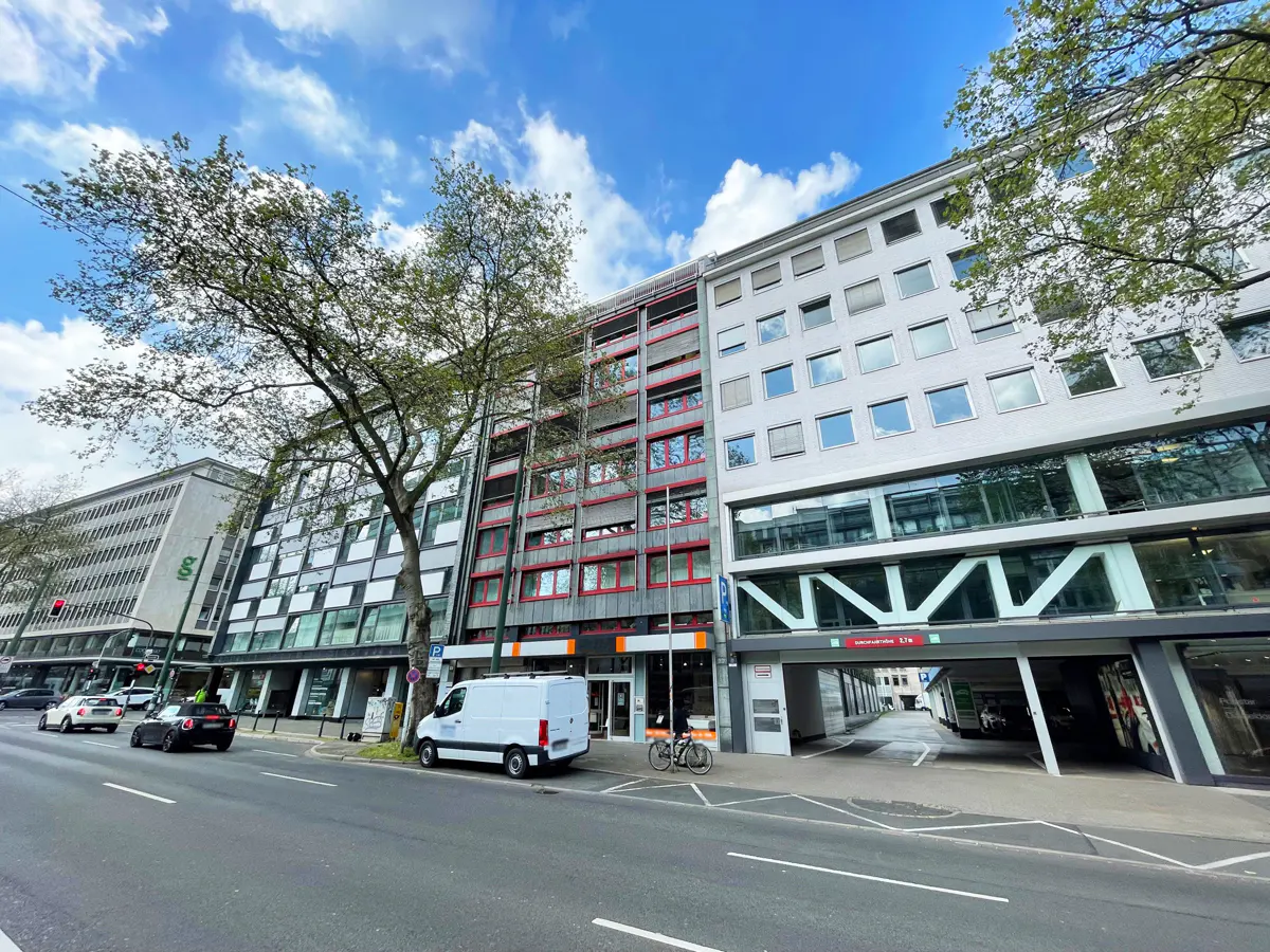 Street view of a row of modern buildings under a blue, cloudy sky. A white van is parked on the side of the road.