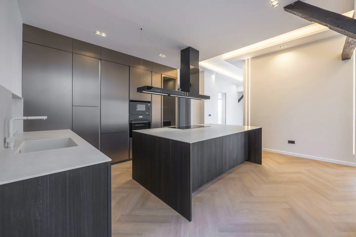 A modern kitchen with stainless steel cabinets, a dark wood island with a white countertop, and herringbone wood floors.