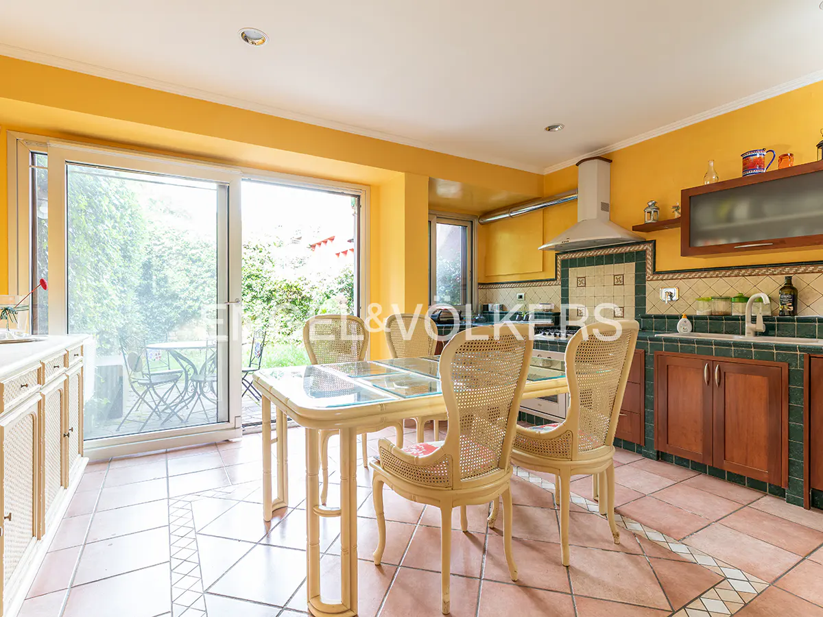 Bright yellow kitchen with a glass-top dining table, rattan chairs, terracotta tile floors, and a view of the garden.