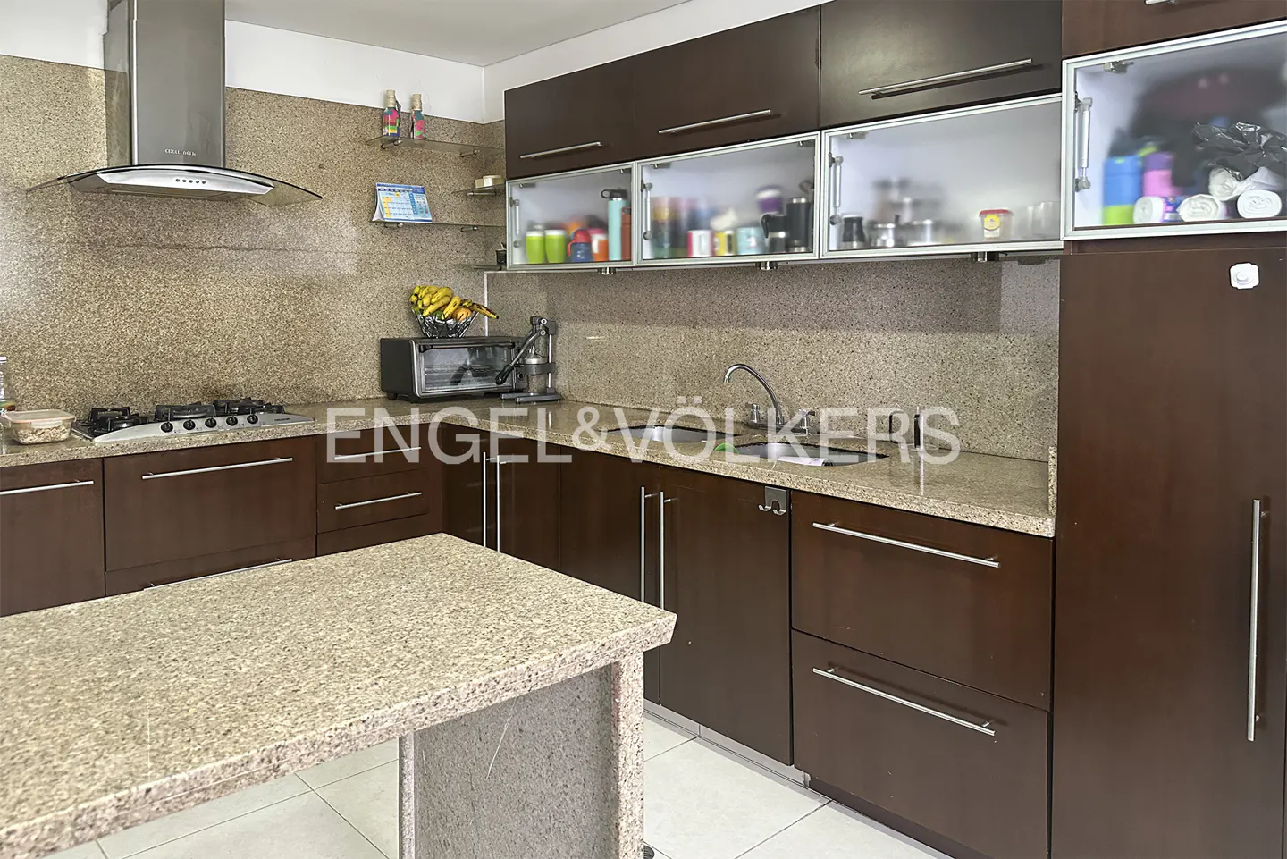 A kitchen with brown cabinets, granite countertops, and stainless steel appliances. A kitchen island is in the foreground.