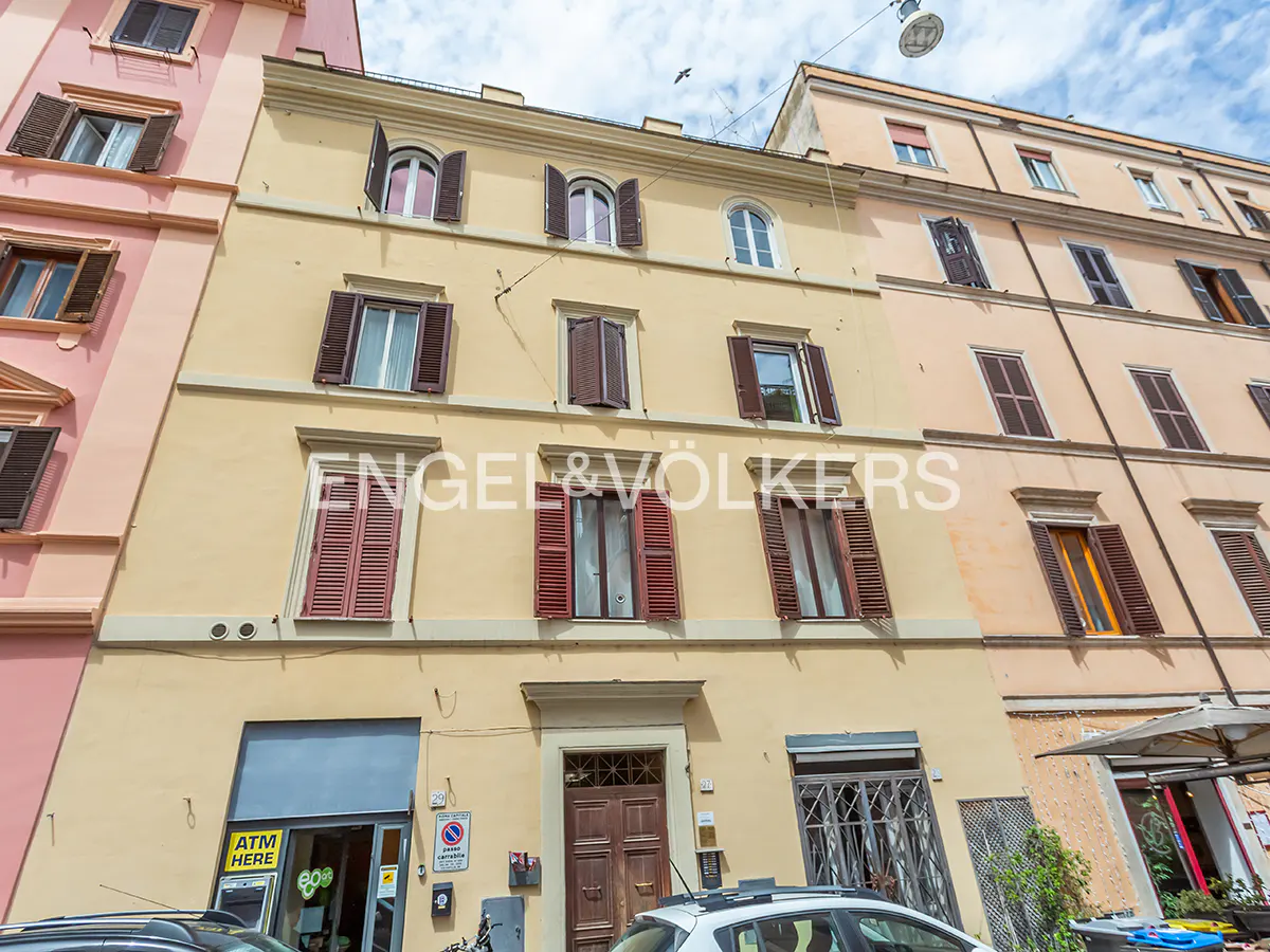 Exterior of a yellow building with brown shutters and an Engel & Völkers sign. Cars are parked in front.