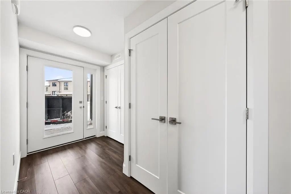Bright entryway with dark wood floors, white walls, and white doors. A glass door leads outside.