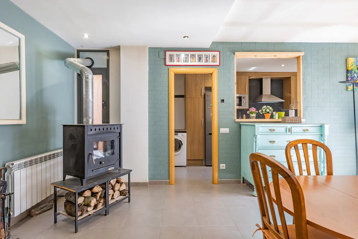 Living room with a wood-burning stove, light blue walls, and a view into the kitchen and laundry room.