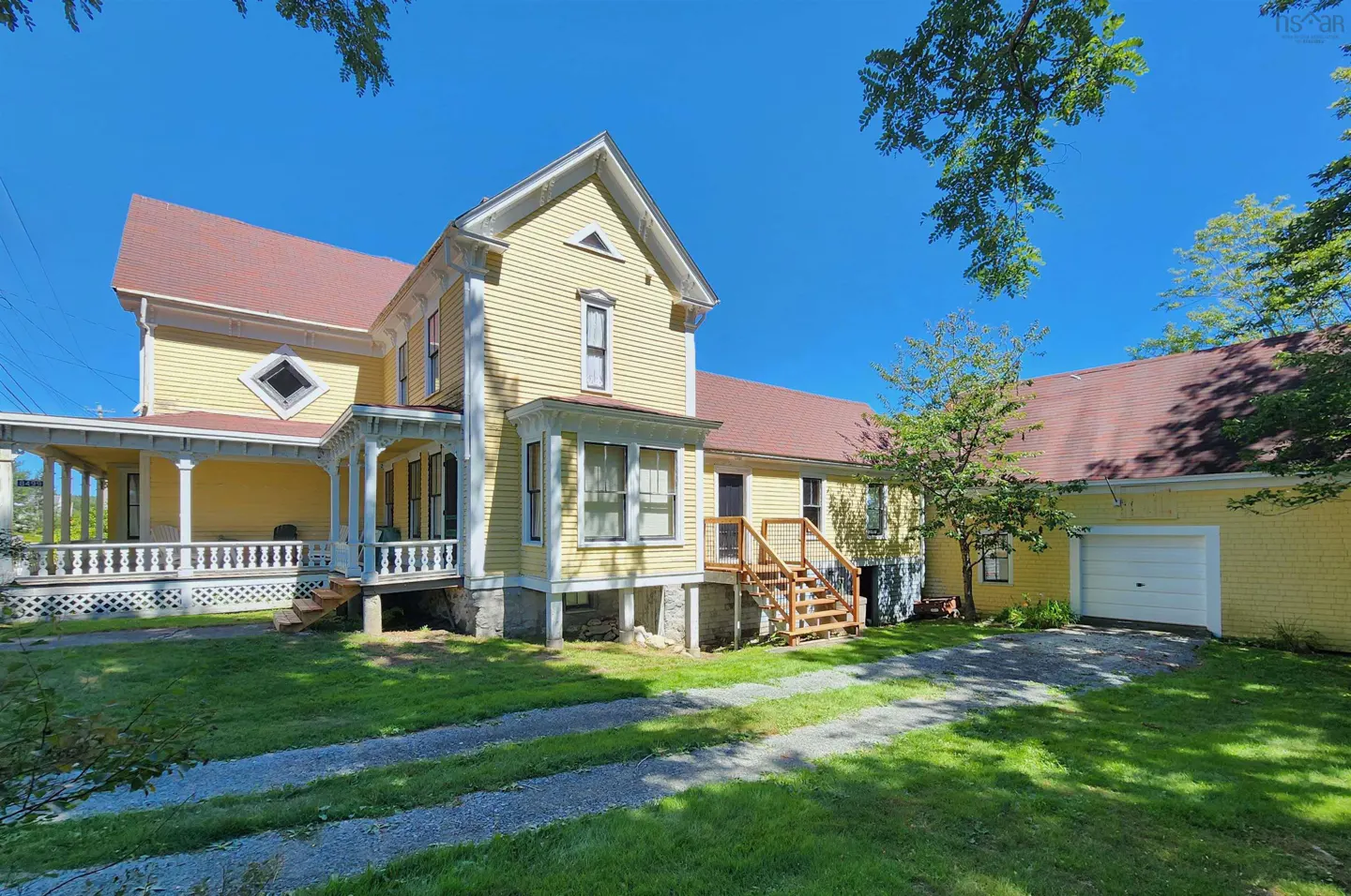 Exterior view of a yellow two-story house with a red roof, a porch, and a garage on a sunny day.
