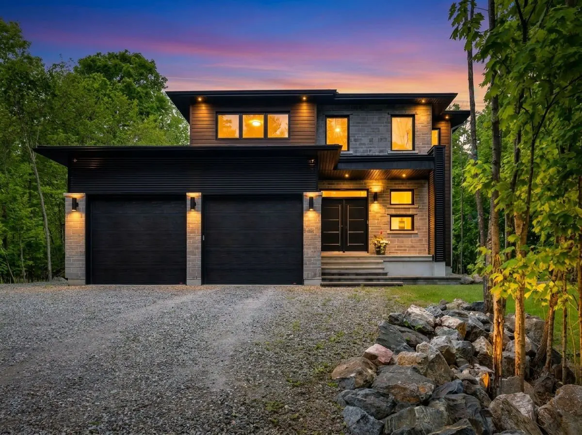 Modern two-story home with black garage doors, stone accents, and warm exterior lighting at sunset.