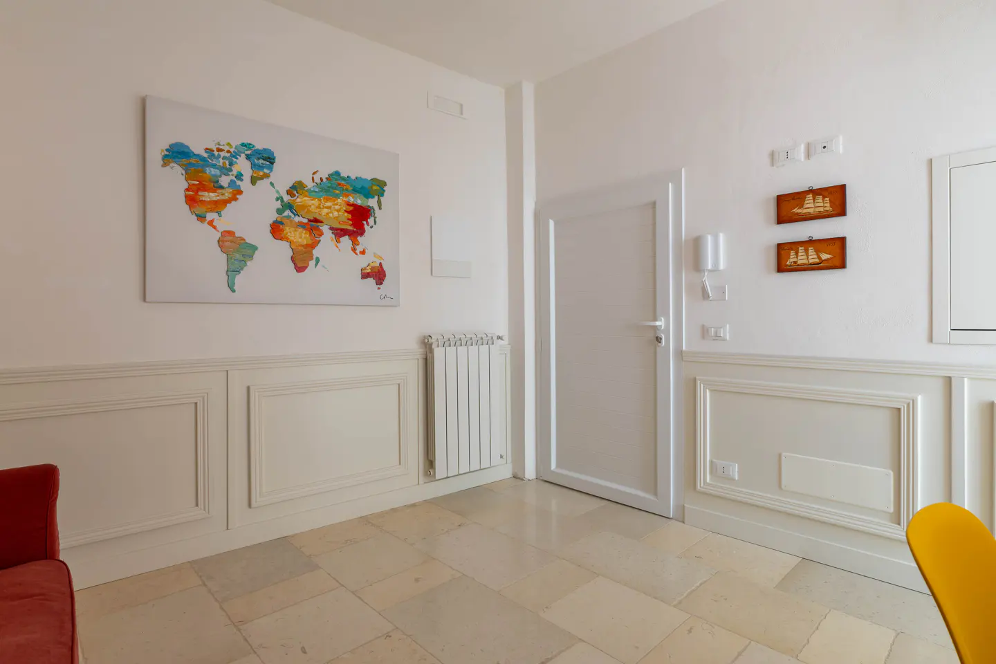 White room with wainscoting, a colorful world map wall art, a white door, and two small framed ship pictures.
