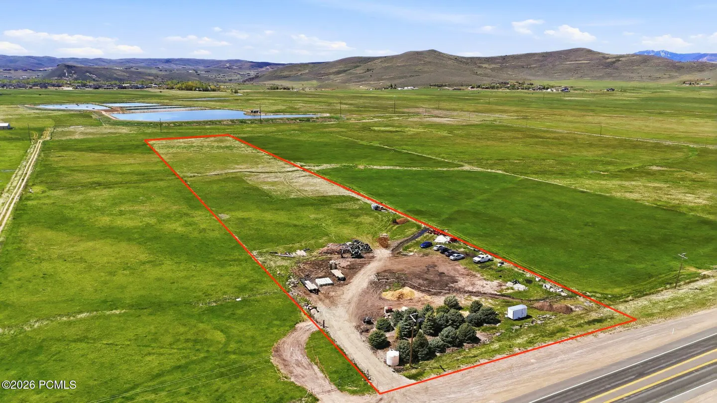 Aerial view of a large, rectangular plot of land outlined in red, with green fields, trees, and mountains in the background.
