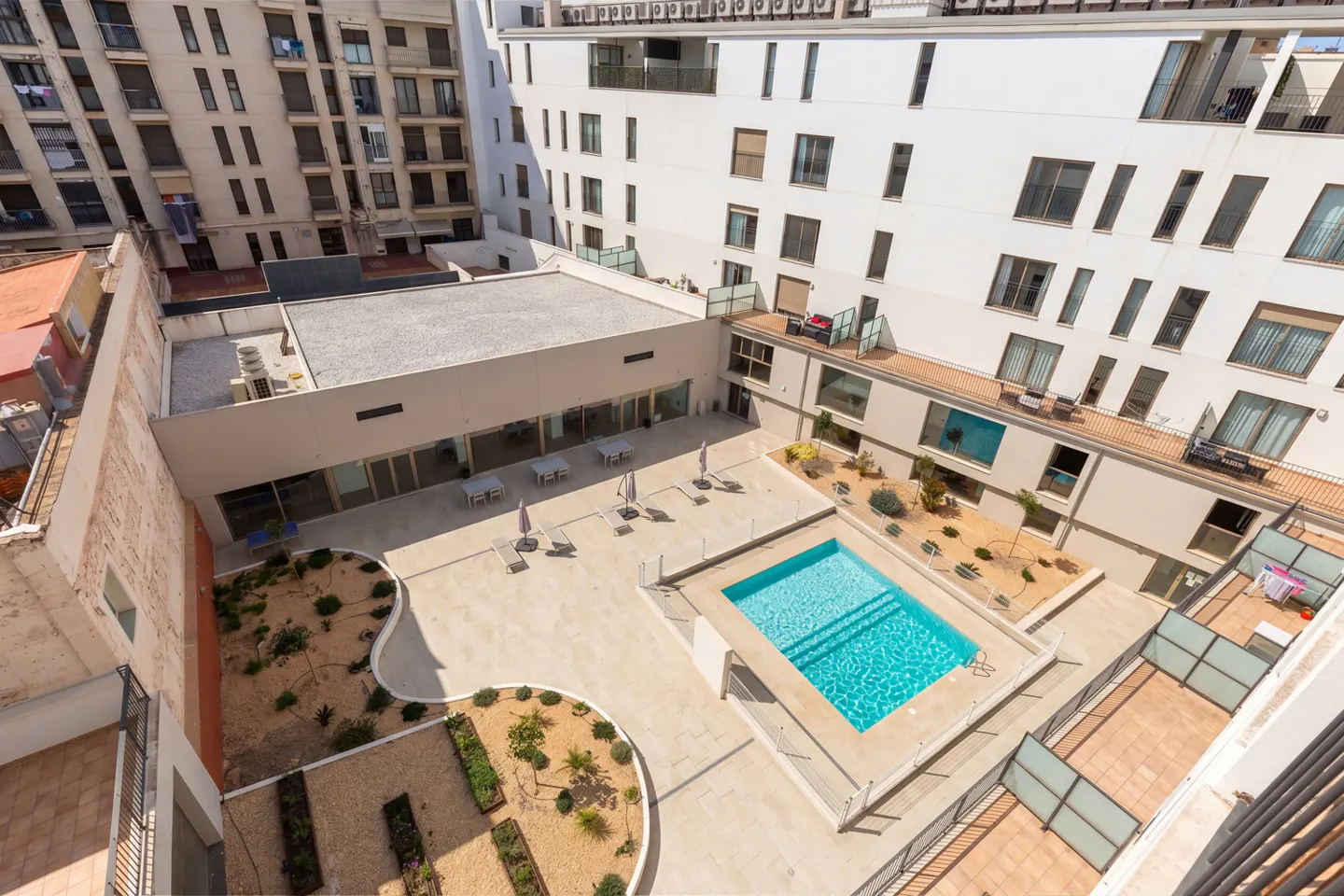 High-angle view of a modern apartment complex courtyard with a swimming pool, landscaped garden beds, and patio seating.
