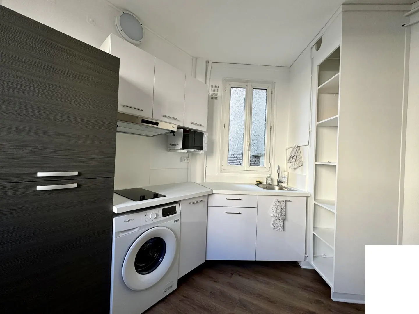 A compact kitchen with white cabinets, a black refrigerator, and a washing machine. A window provides natural light.