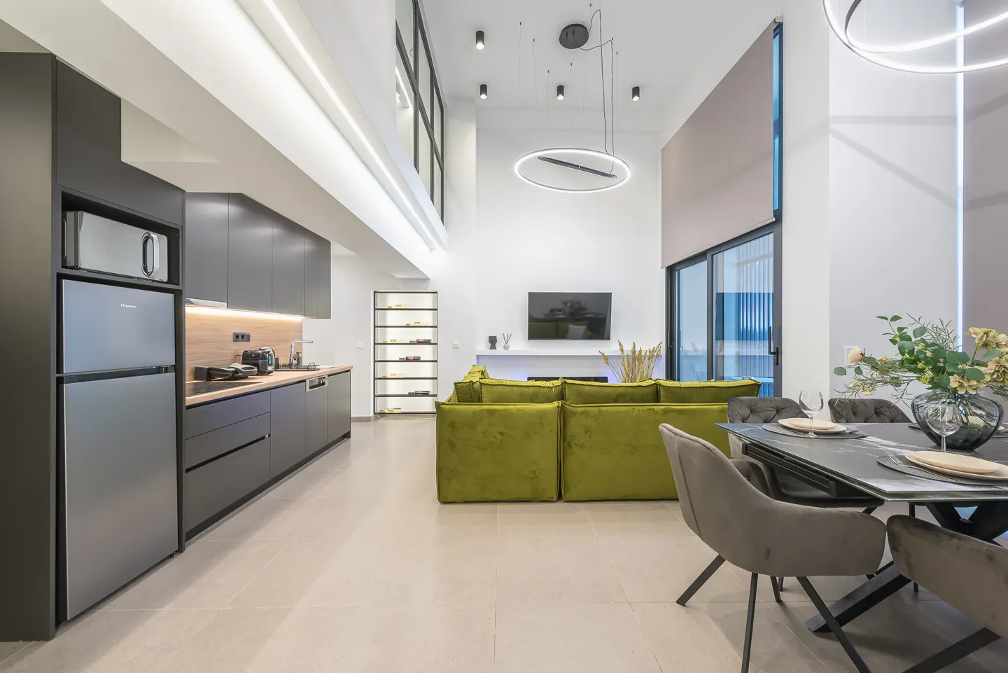 A modern, open-concept living space with a gray kitchen, green sofa, and dining table with gray chairs.