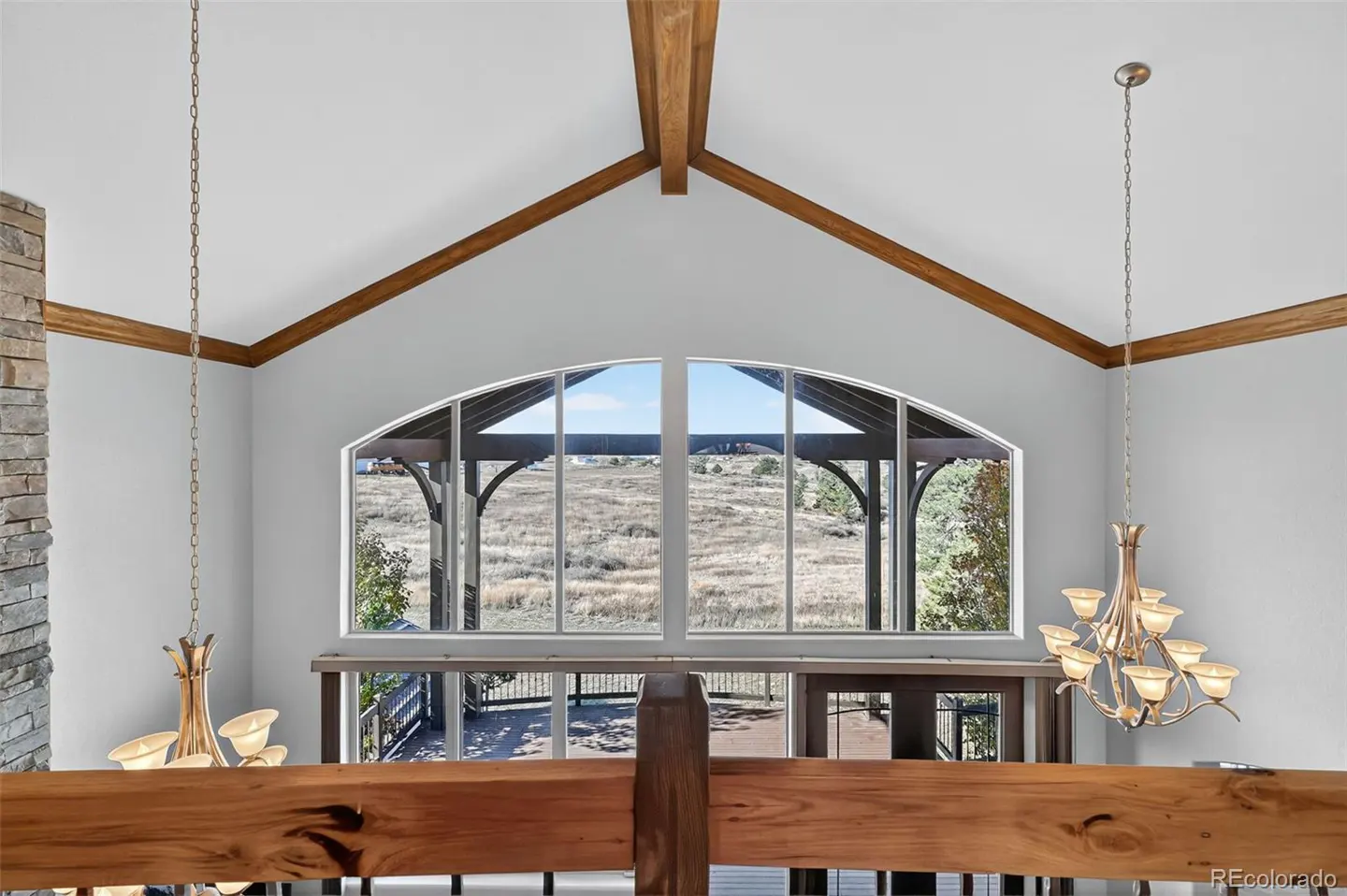 Interior view of a home featuring a large arched window with a view of a field, wooden beams, and chandeliers.