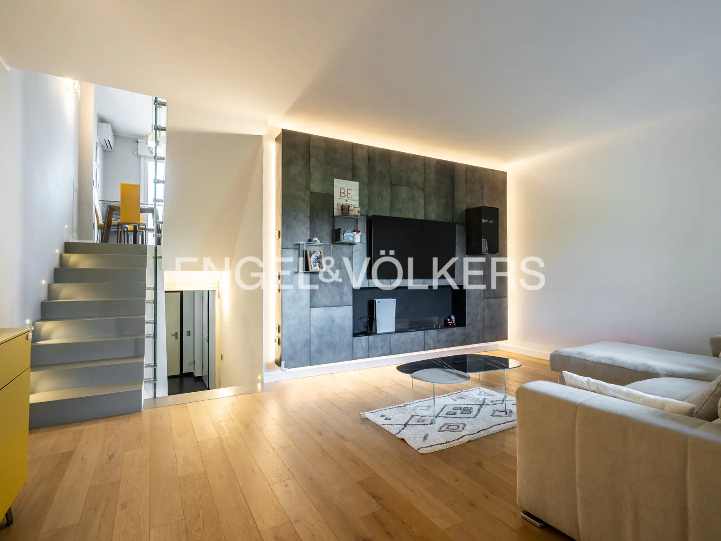 Living room with hardwood floors, gray accent wall with TV, and a gray staircase with yellow cabinet.