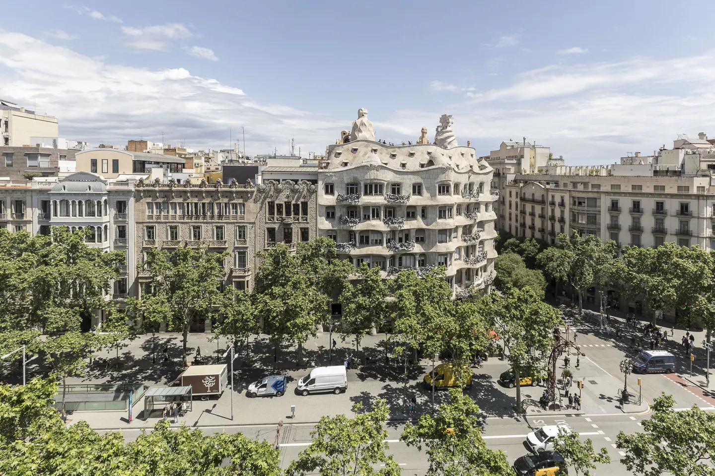 Barcelona cityscape featuring Casa Milà, a modernist building, with trees and traffic below on a sunny day.
