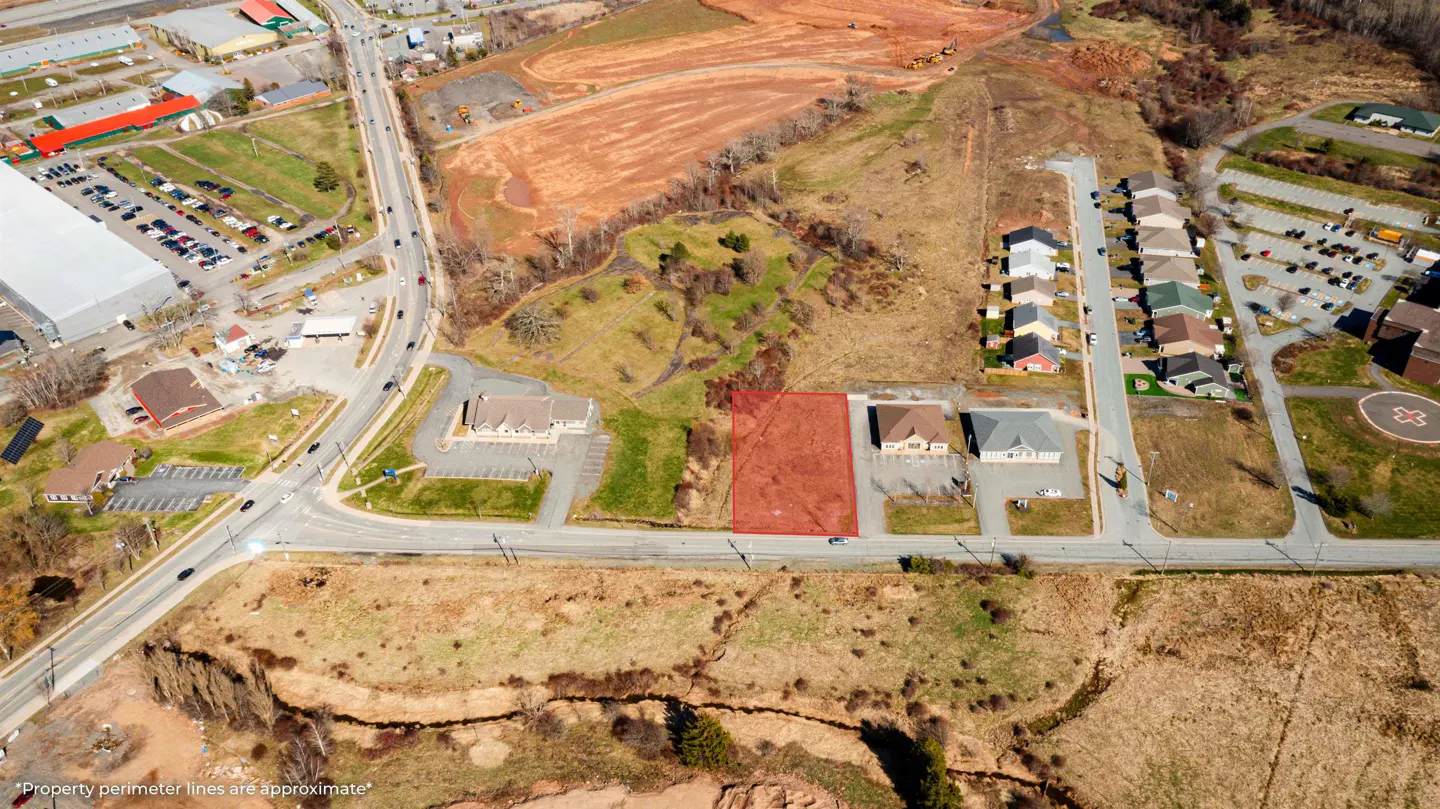 Aerial view of a vacant lot outlined in red, situated between two commercial buildings on a road with surrounding buildings and parking lots.