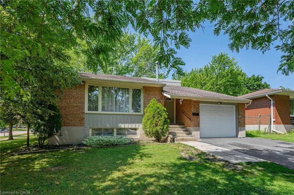 A single-story brick house with a white garage door, green lawn, and trees.