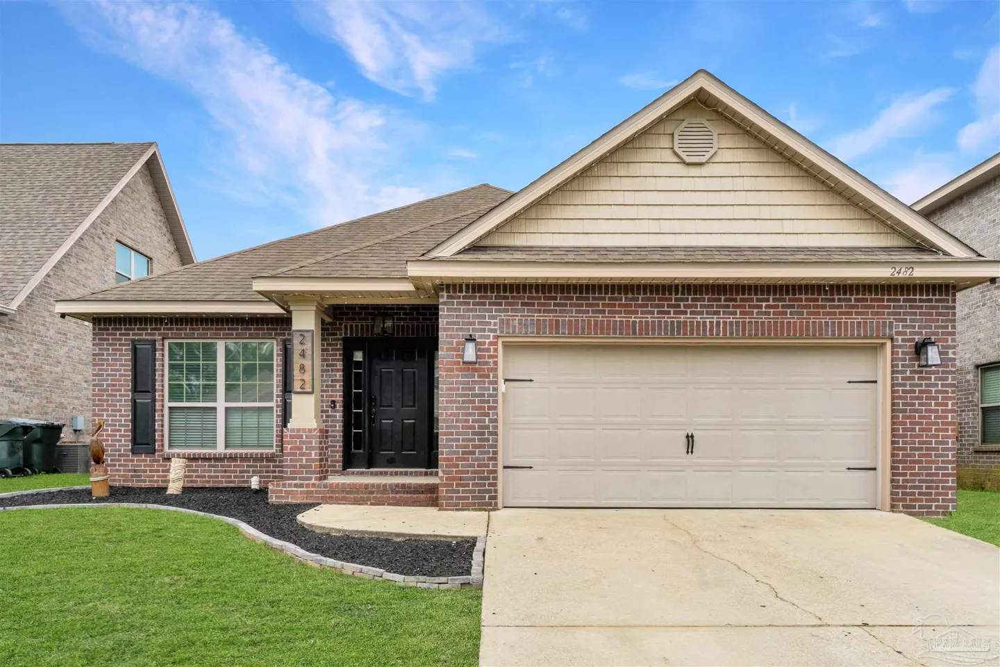 A single-story brick house with a beige garage door and a black front door under a blue sky.
