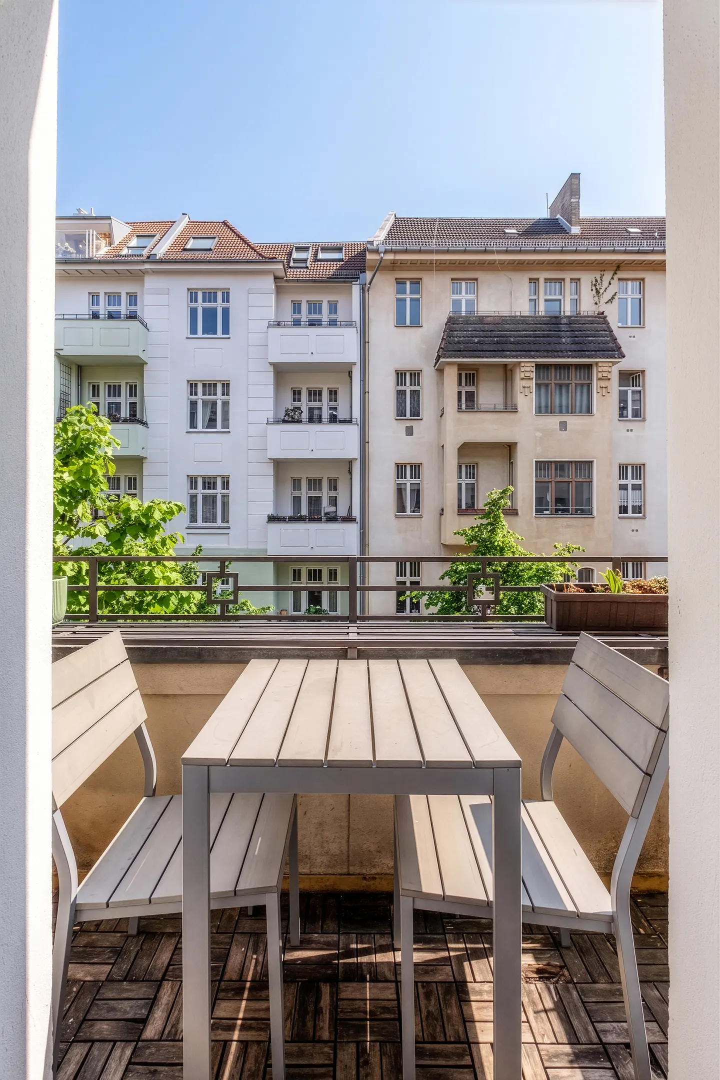 A balcony with a light-colored table and two chairs overlooking a city street with white and beige apartment buildings.