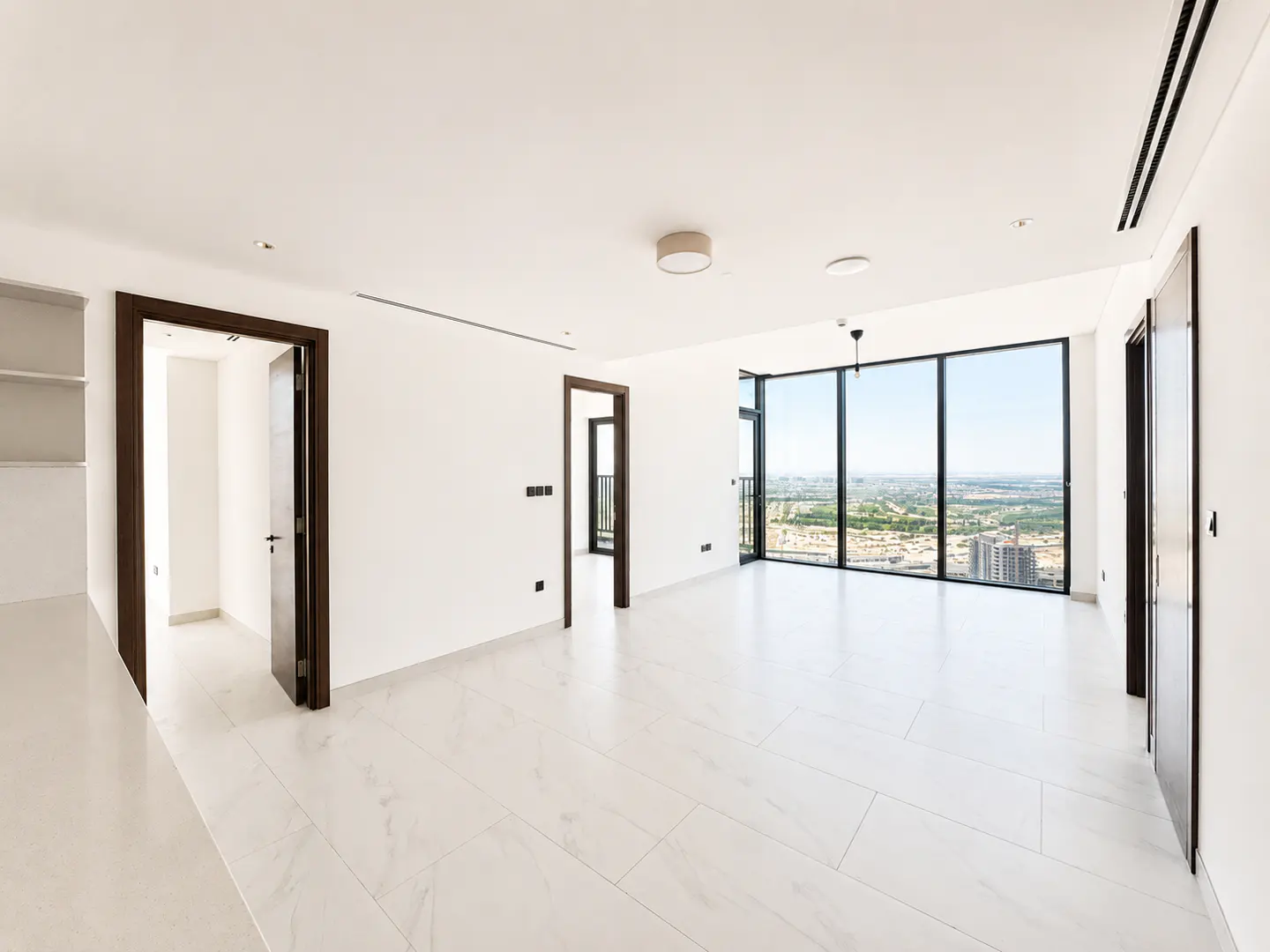 Bright, empty room with white walls, marble floors, and a large window showing a city view. Dark wood doors and trim add contrast.