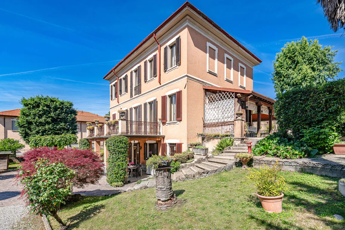 A three-story peach-colored villa with brown shutters, a balcony, and a stone staircase leading to a garden patio.