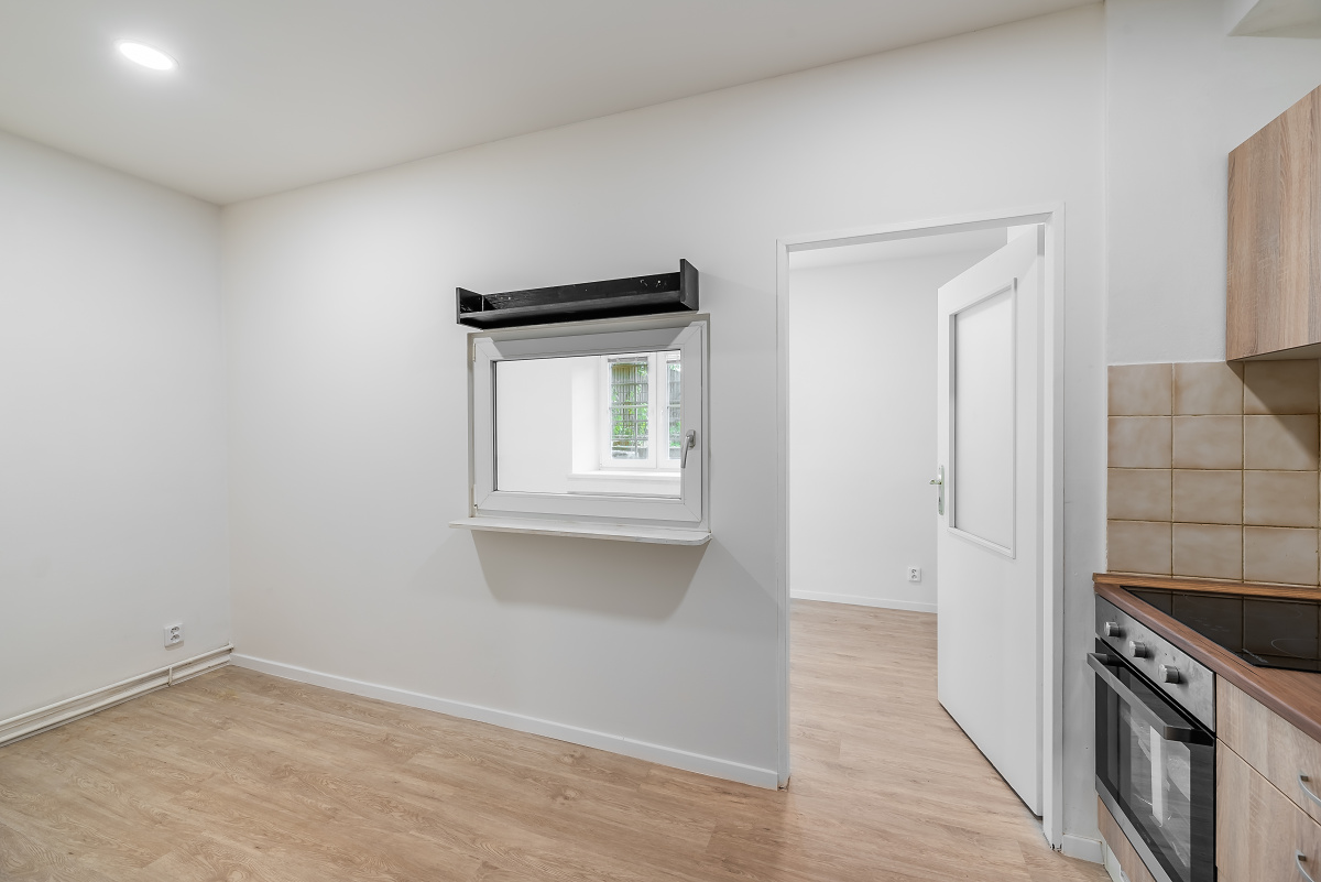 Bright room with light wood floors, a white wall featuring a small interior window, and a doorway to an adjacent room. [AI-generated text]
