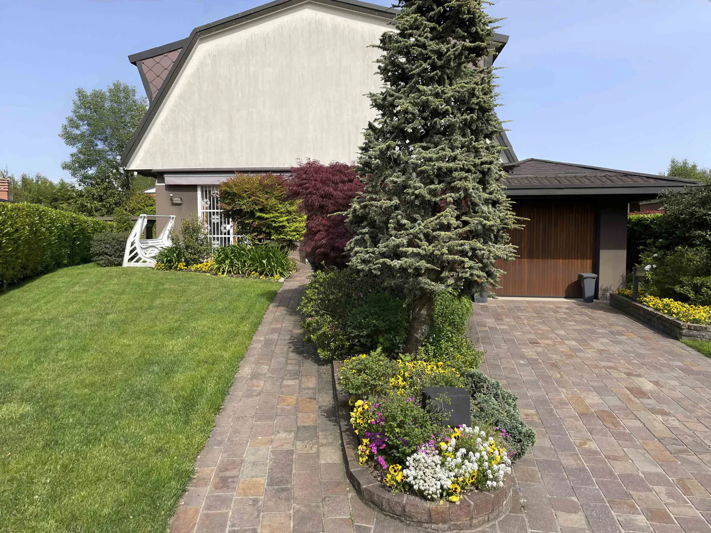 Exterior view of a two-story house with a green lawn, brick driveway, and well-maintained landscaping.