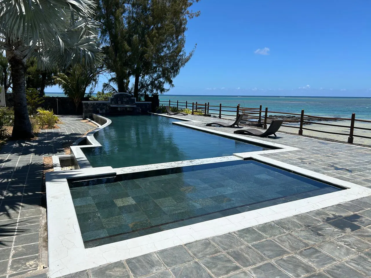 A luxurious pool with lounge chairs overlooks a sandy beach and turquoise ocean under a clear blue sky.