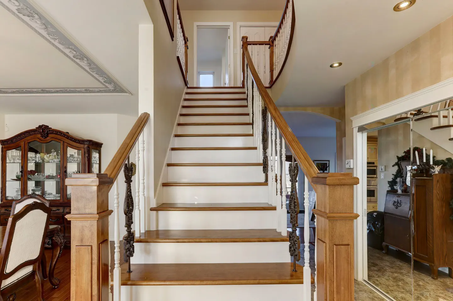 Interior view of a staircase with wood treads and white risers, leading to an upper level. Wood railing with decorative ironwork.