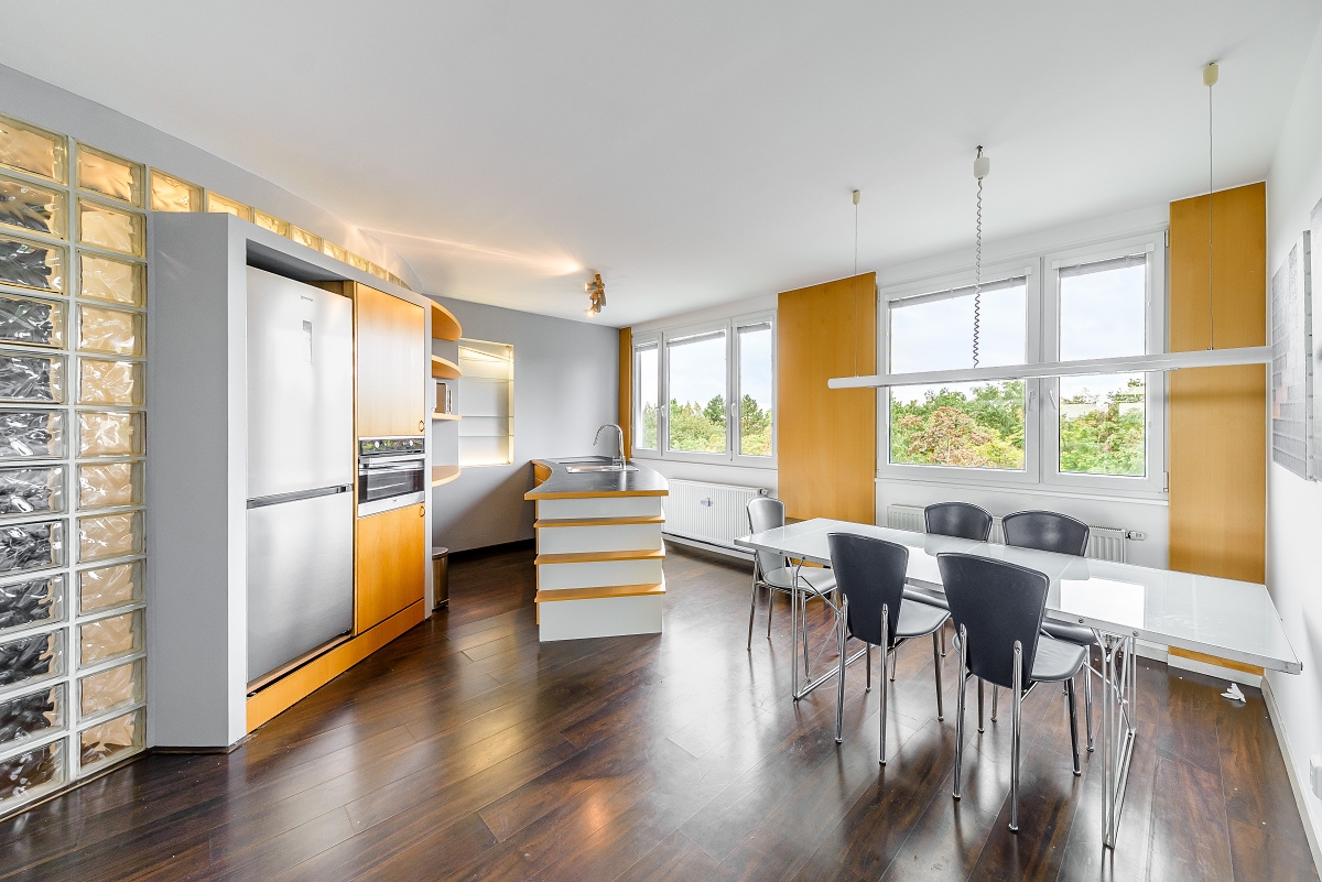 Modern kitchen with wood cabinets, stainless steel fridge, glass block wall, and dining table with chairs on wood floors.