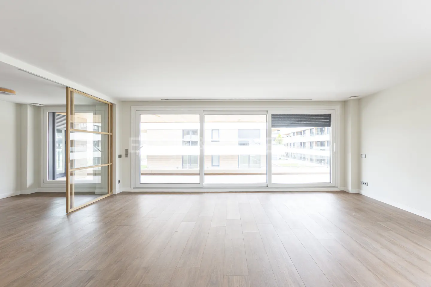 Bright, empty room with light wood floors, white walls, and large sliding glass doors leading to a balcony.