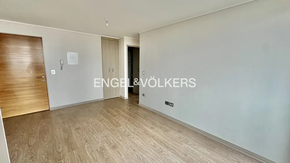 Empty room with wood-look floors, light gray walls, and a wood door. Engel & Völkers logo is superimposed on the wall.