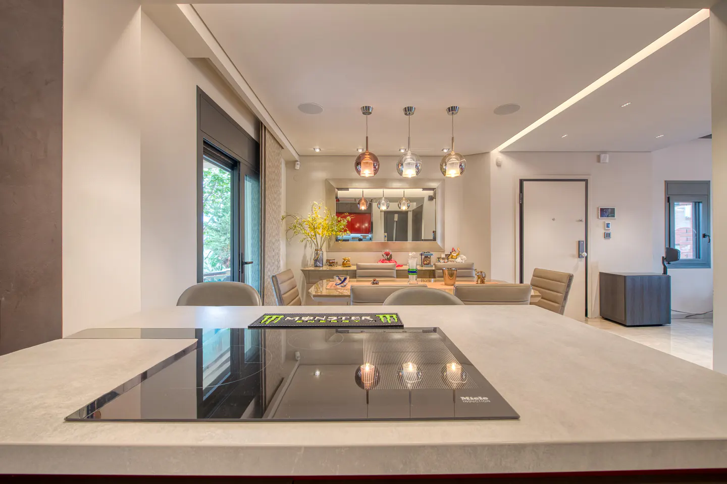 Modern kitchen island with a black induction cooktop, overlooking a dining area with pendant lights and beige chairs.