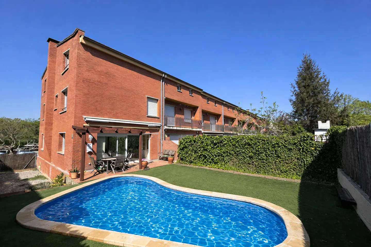 A brick house with a blue kidney-shaped pool in the backyard under a clear blue sky.